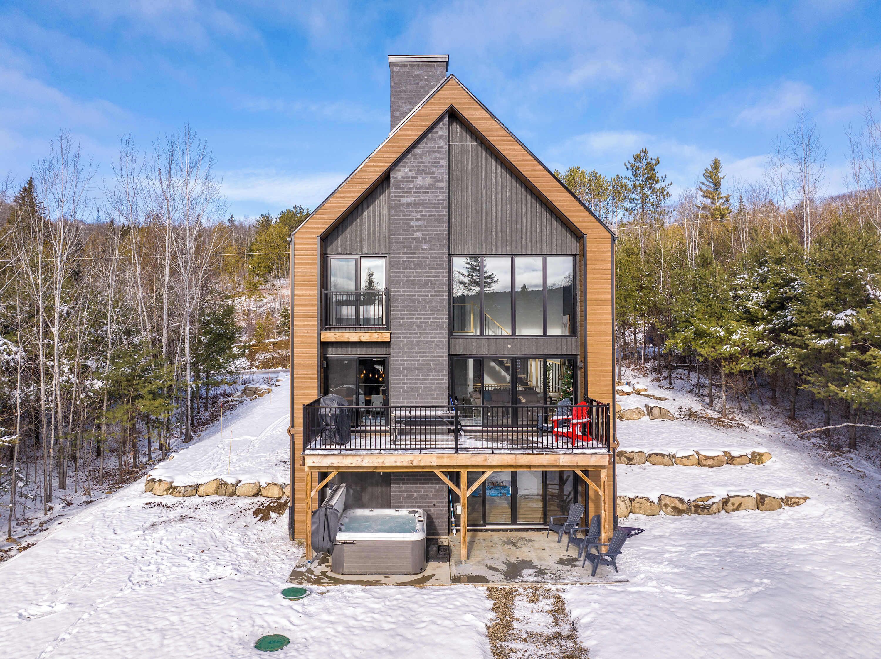 Une cabane moderne à deux étages, dotée d’un balcon, d’un jacuzzi et de fondations en pierre.