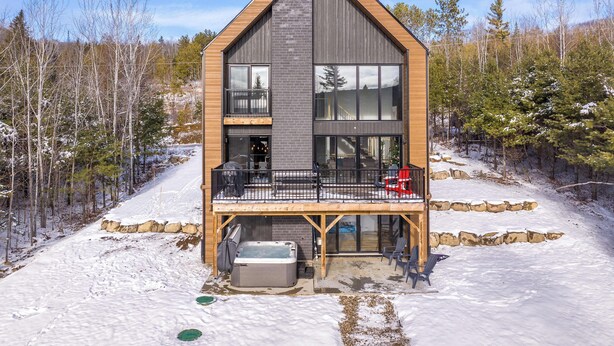 A modern two-story cabin with a balcony, a hot tub, and a stone foundation. - Scandinavian chalet | SPA and Pool Table | Le 70 (Lanaudière)