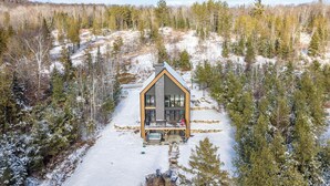 A modern cabin with a large balcony, surrounded by a snowy forest. - Scandinavian chalet | SPA and Pool Table | Le 70 (Lanaudière)