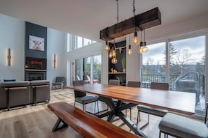 A modern living room with a wooden dining table, grey sofas, and a fireplace.