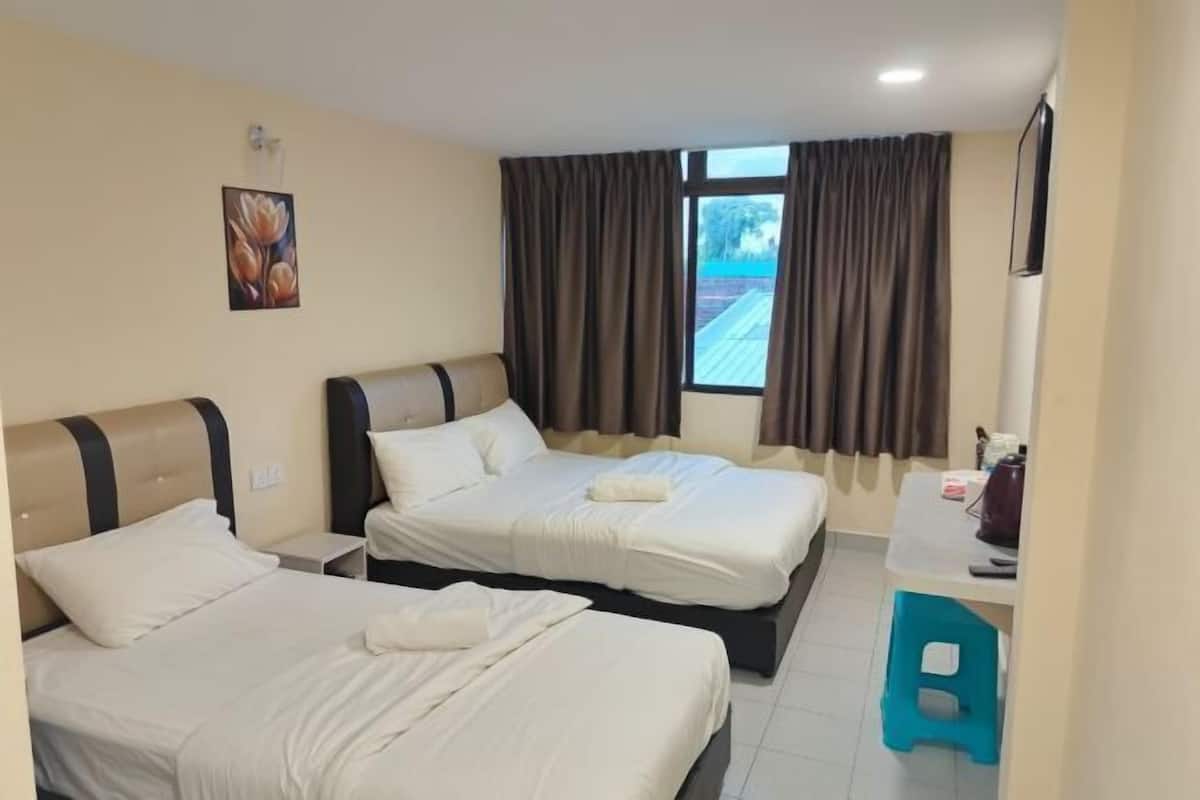 A hotel room with two beds, a small desk, a chair, and a window with curtains.