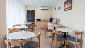 A dining area with round tables and chairs, a kitchen in the background, and a door leading to another room. - Southern TIP Hotel (Pontian District)