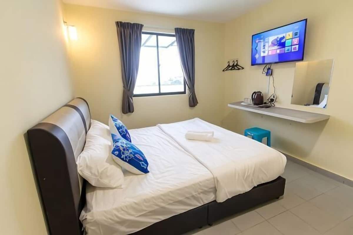 A bedroom with a bed, a television, a window with curtains, and a small table with a cup.
