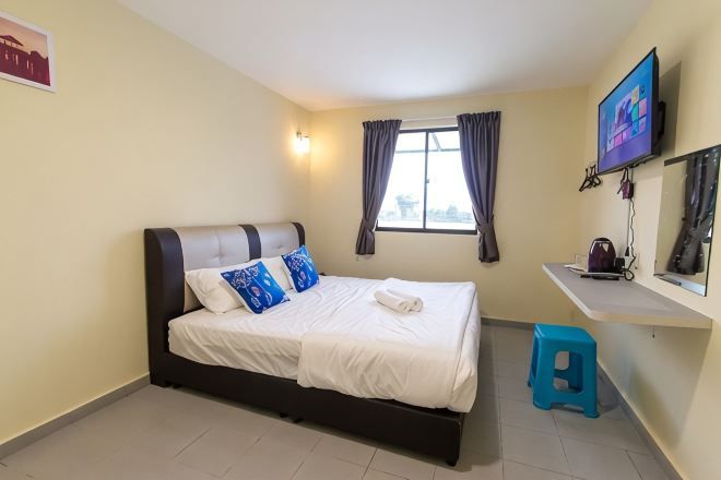 A bedroom with a bed, a TV, a window with curtains, and a small stool.