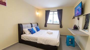 A bedroom with a bed, a TV, a window with curtains, and a small stool.