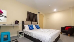A bedroom with a bed, a nightstand, a chair, and a desk with a chair. - Southern TIP Hotel (Pontian District)
