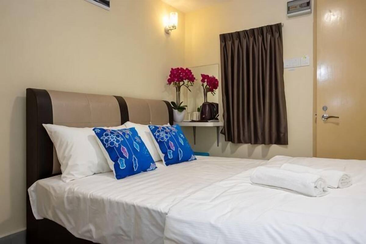 A hotel room with a bed, pillows, a nightstand, a mirror, a vase with flowers, and a door.