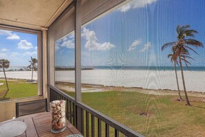 A room with a large window overlooking a beach, a wooden table, and a glass vase with shells.