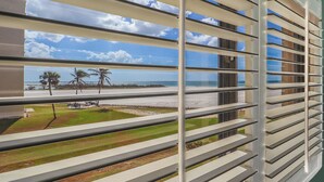 A view through window blinds to a beach with palm trees and a clear sky. - Beachfront 2B/2B Sandarac Vacation Condo - Million Dollar Gulf View! (Fort Myers Beach)