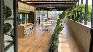 Un comedor interior con suelo de madera, sillas blancas y una mesa larga. Amplias ventanas permiten la entrada de luz natural y vistas al exterior.