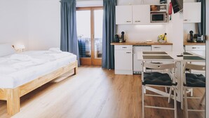 A modern hotel room with a wooden bed, a kitchenette, and a view through a glass door. - Apartments Haus Altenberger 1 Studio (Zell am See)