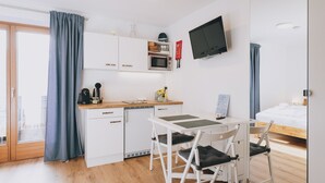 A compact room with a kitchenette, a flat-screen TV, a bed, and a sliding glass door to the outside. - Apartments Haus Altenberger 1 Studio (Zell am See)