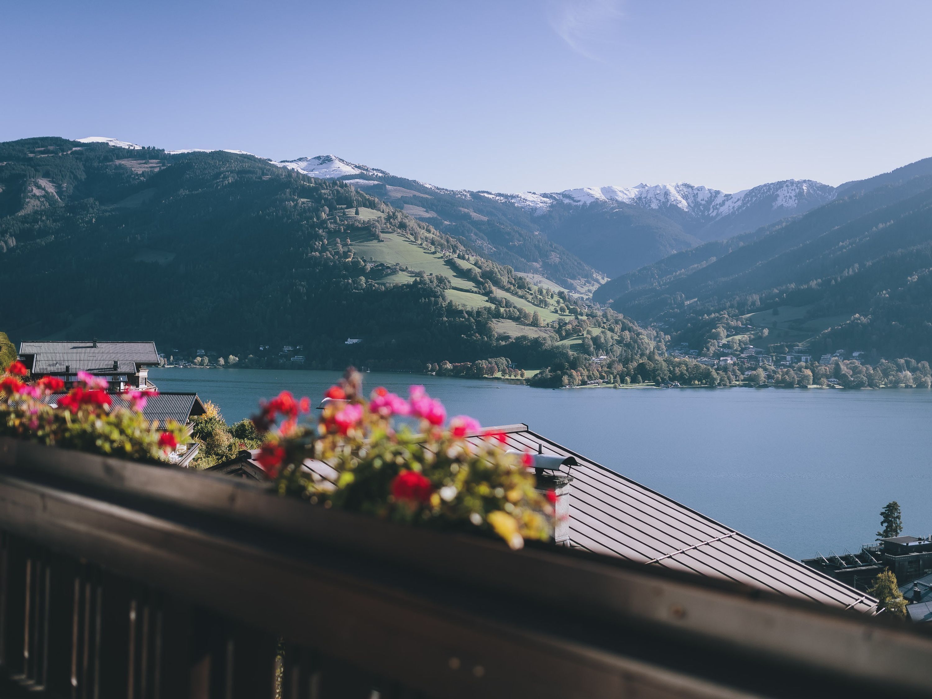 Une vue pittoresque d’un lac, avec des montagnes en arrière-plan, un balcon en bois orné de fleurs et un ciel dégagé.