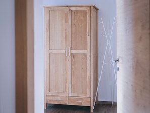 A wooden wardrobe with two doors and two drawers, positioned in a hallway with a white wall and a wooden floor.