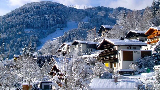 A snow-covered mountain village with traditional wooden houses, a ski slope in the background, and a clear sky. - Apartments Haus Altenberger 4 Seeblick (Zell am See)