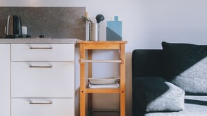 Una kitchenette con cafetera, repisa con utensilios de cocina y un pequeño estante de madera con un bol y una bandeja.