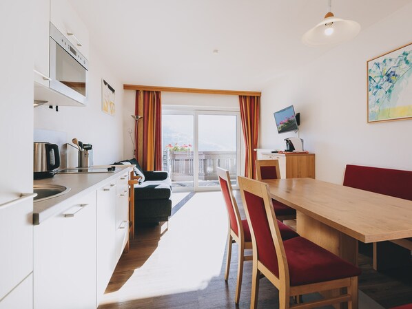 Une cuisine moderne avec un coin repas, un téléviseur et un balcon agrémenté de rideaux.