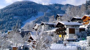 Un pueblo cubierto de nieve con casas de madera tradicionales, una pista de esquí al fondo y un cielo despejado.