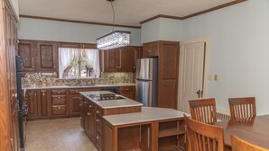 Una cocina con armarios de madera, un refrigerador de acero inoxidable, una mesa de comedor con sillas y un candelabro.