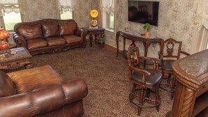 Una sala de estar con un sofá de cuero marrón, sillas de madera, una mesa de madera y un televisor montado en la pared.