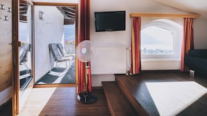 Un salon confortable avec un téléviseur, un ventilateur et une vue sur les montagnes, visible à travers une grande fenêtre.
