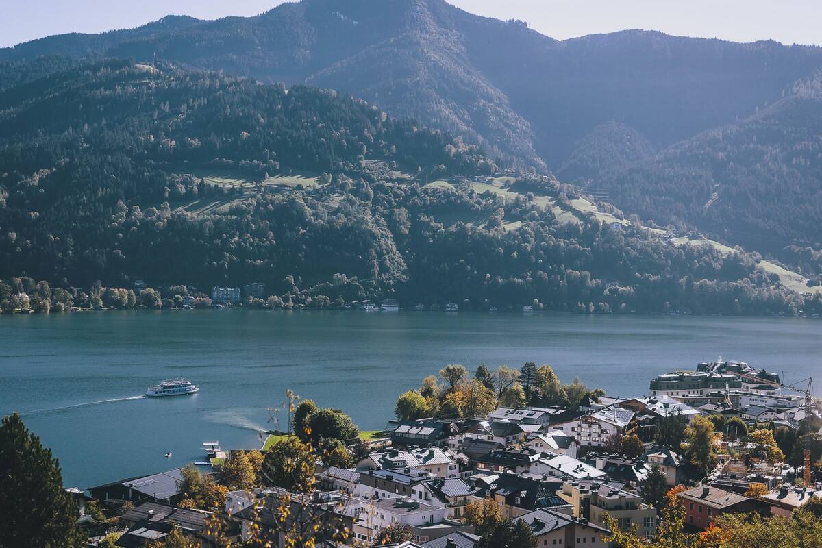 A lakeside town with buildings, a boat on the water, and mountains in the background.