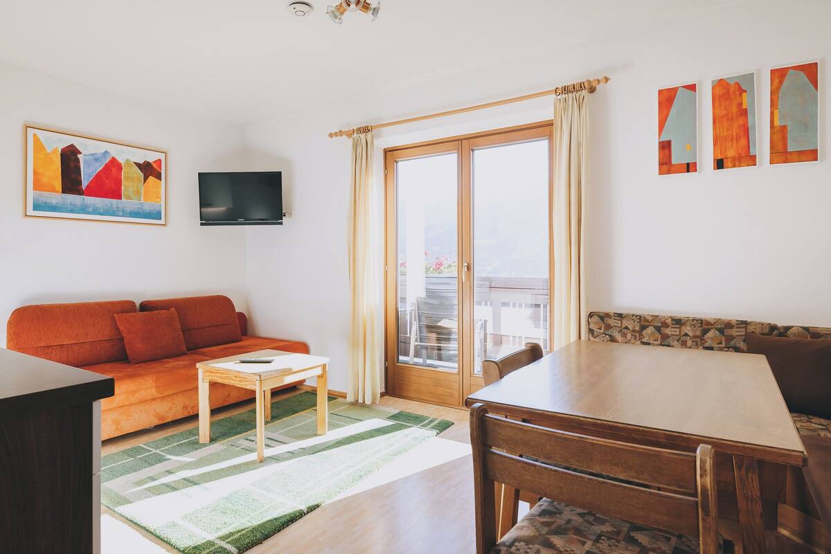 A living room with a sofa, a small table, a TV, and a balcony with curtains.
