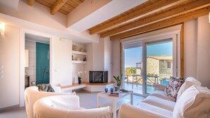 Una sala de estar moderna con muebles blancos, un televisor y un balcón con vistas al campo.