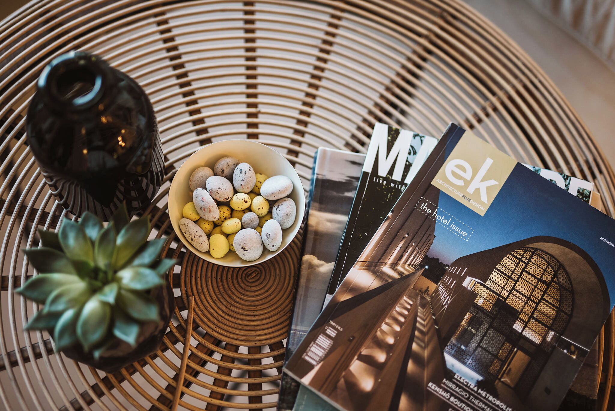 A wicker table with a bowl of decorative eggs, a succulent plant, and a magazine titled "ek".