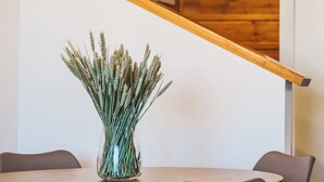 Un área de comedor con escalera de madera, un jarrón con plantas secas y bombillas colgantes.