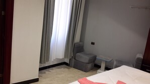 Ein Hotelzimmer mit einem Bett, einem kleinen Tisch, einem Stuhl und einem Fenster mit Vorhängen.