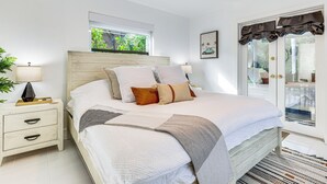 Ein ordentlich eingerichtetes Schlafzimmer mit Bett, Nachttischen, einem Fenster mit Aussicht und einer Tür mit Vorhängen.