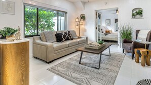 Ein modernes Wohnzimmer mit einer Couch, einem Couchtisch und einem Beistelltisch. Ein großes Fenster bietet Blick auf Grünfläche.