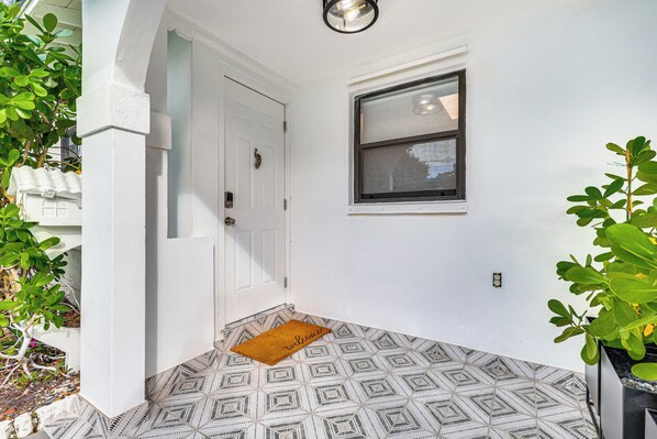 A clean, white-walled entrance with a geometric patterned floor, a small window, and a welcome mat.