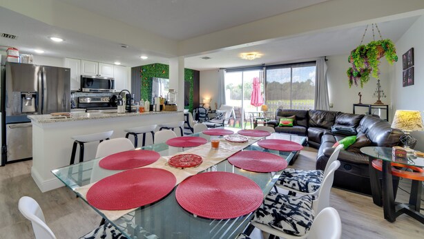 Eine moderne Küche mit Edelstahlgeräten, ein Essbereich mit roten Untersetzern und ein Wohnzimmer mit einer Ledersofa und einer hängenden Pflanze.