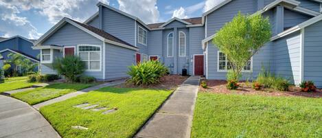 A row of blue houses with red doors, green lawns, and a clear sky.