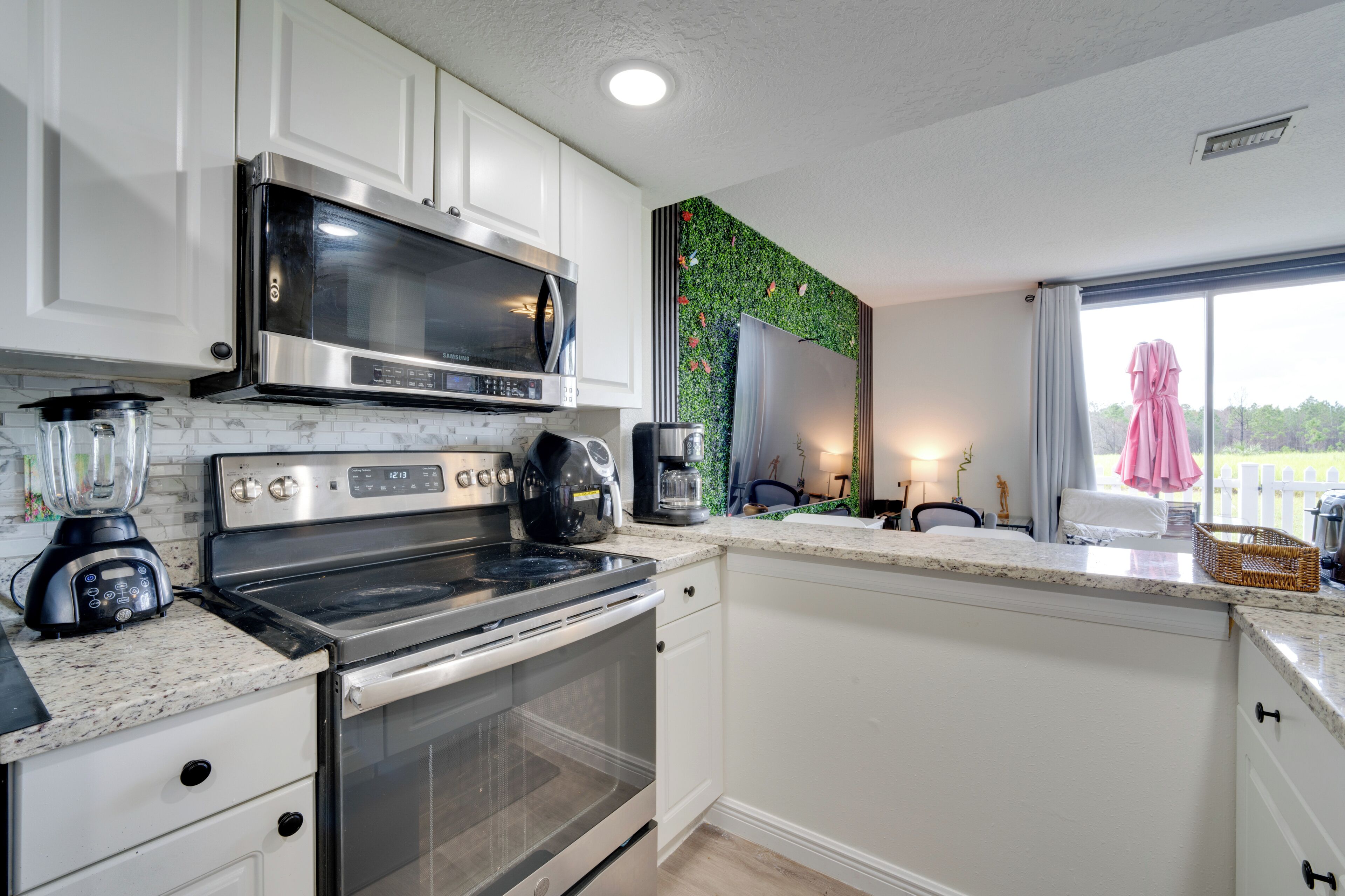 A modern kitchen with white cabinets, stainless steel appliances, a built-in microwave, and a large window with a view of greenery.