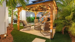 A covered outdoor seating area with chairs and a table, surrounded by greenery and a staircase. - Pool, Mini Golf & Cabana: Bradenton Retreat (Bradenton)