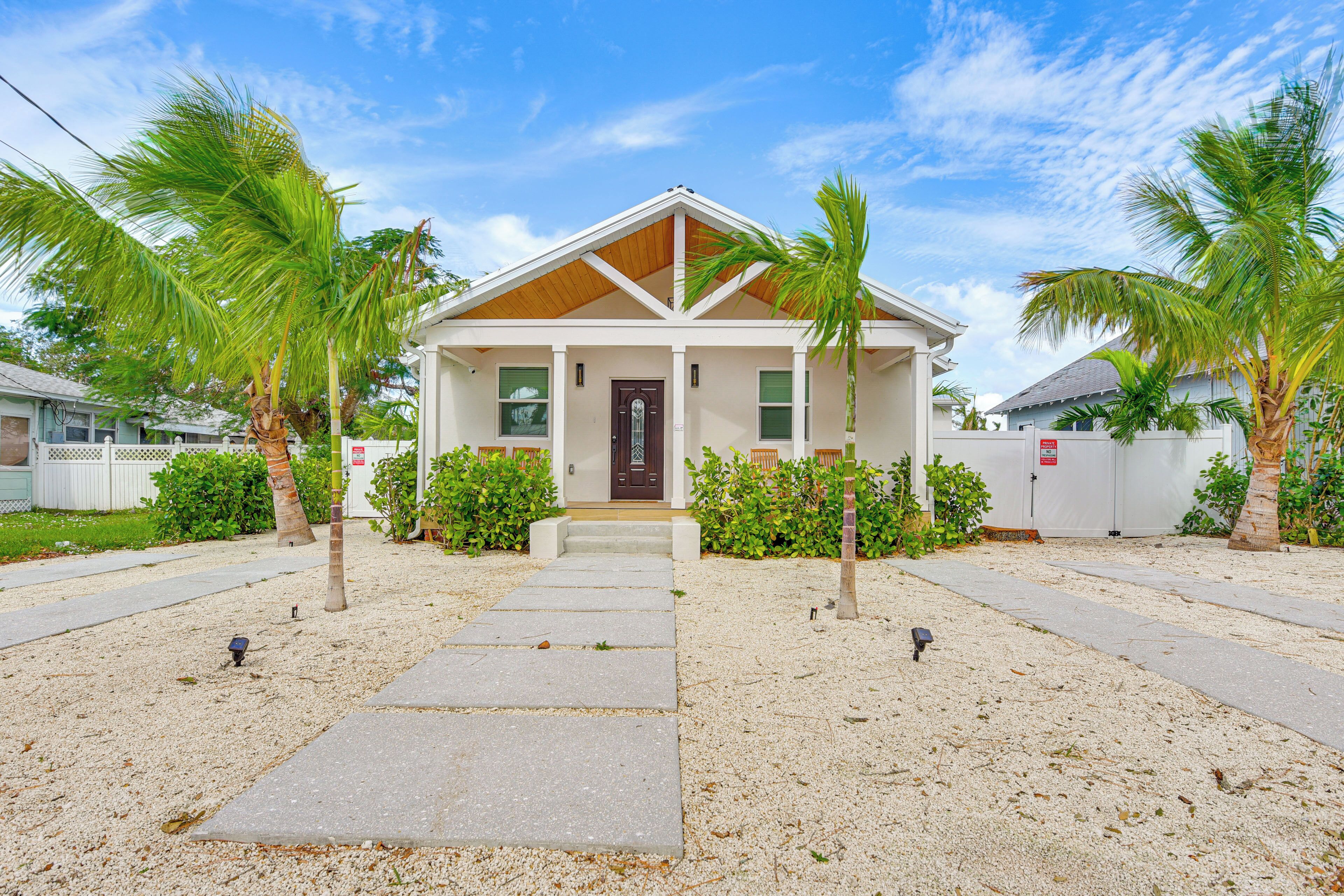 A two-story house with a front porch, palm trees, and a clear sky.