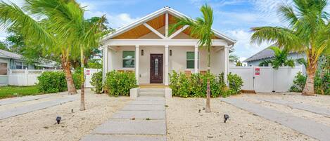 A two-story house with a front porch, palm trees, and a clear sky.