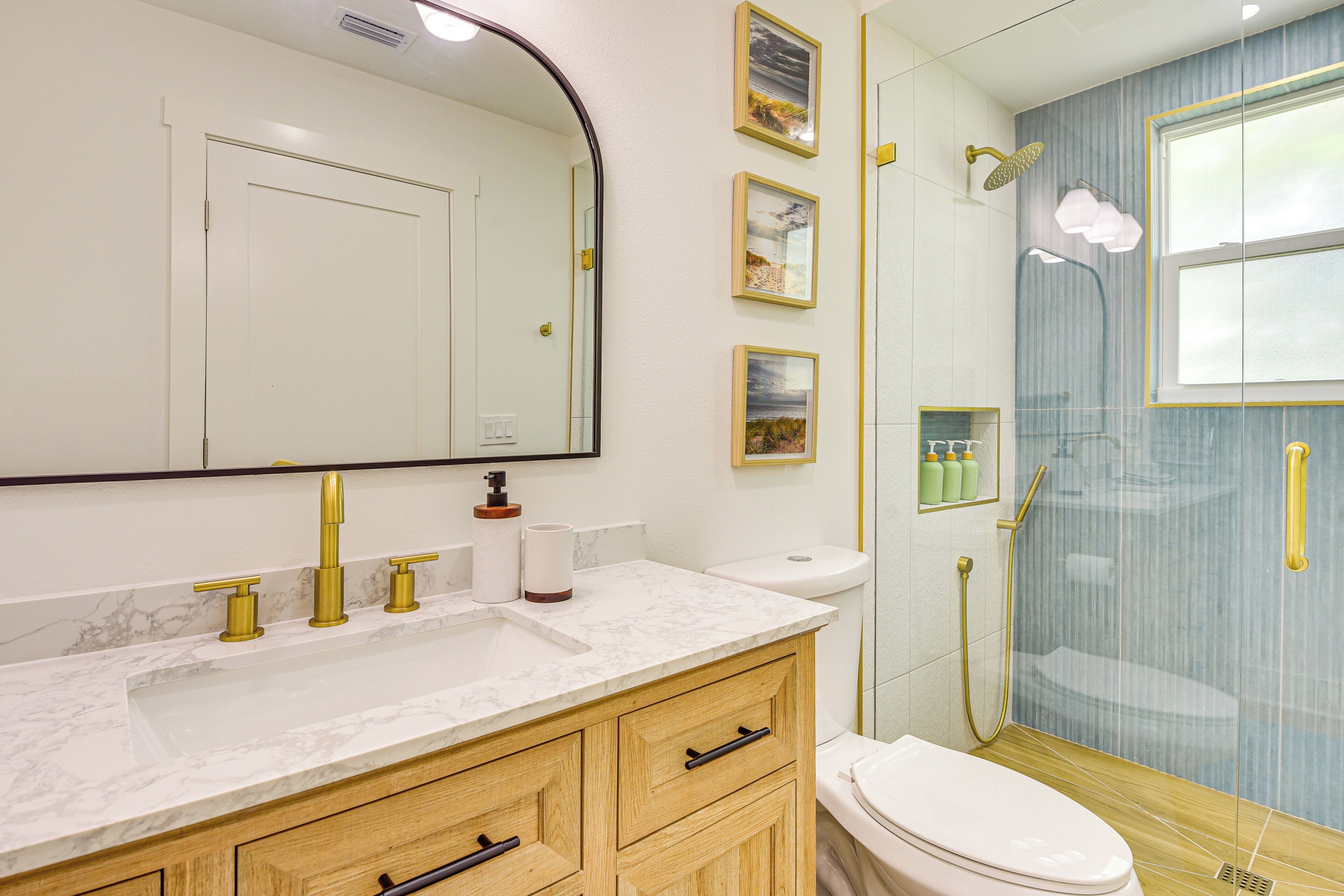 A bathroom with a marble sink, wooden vanity, a toilet, and a glass-enclosed shower.