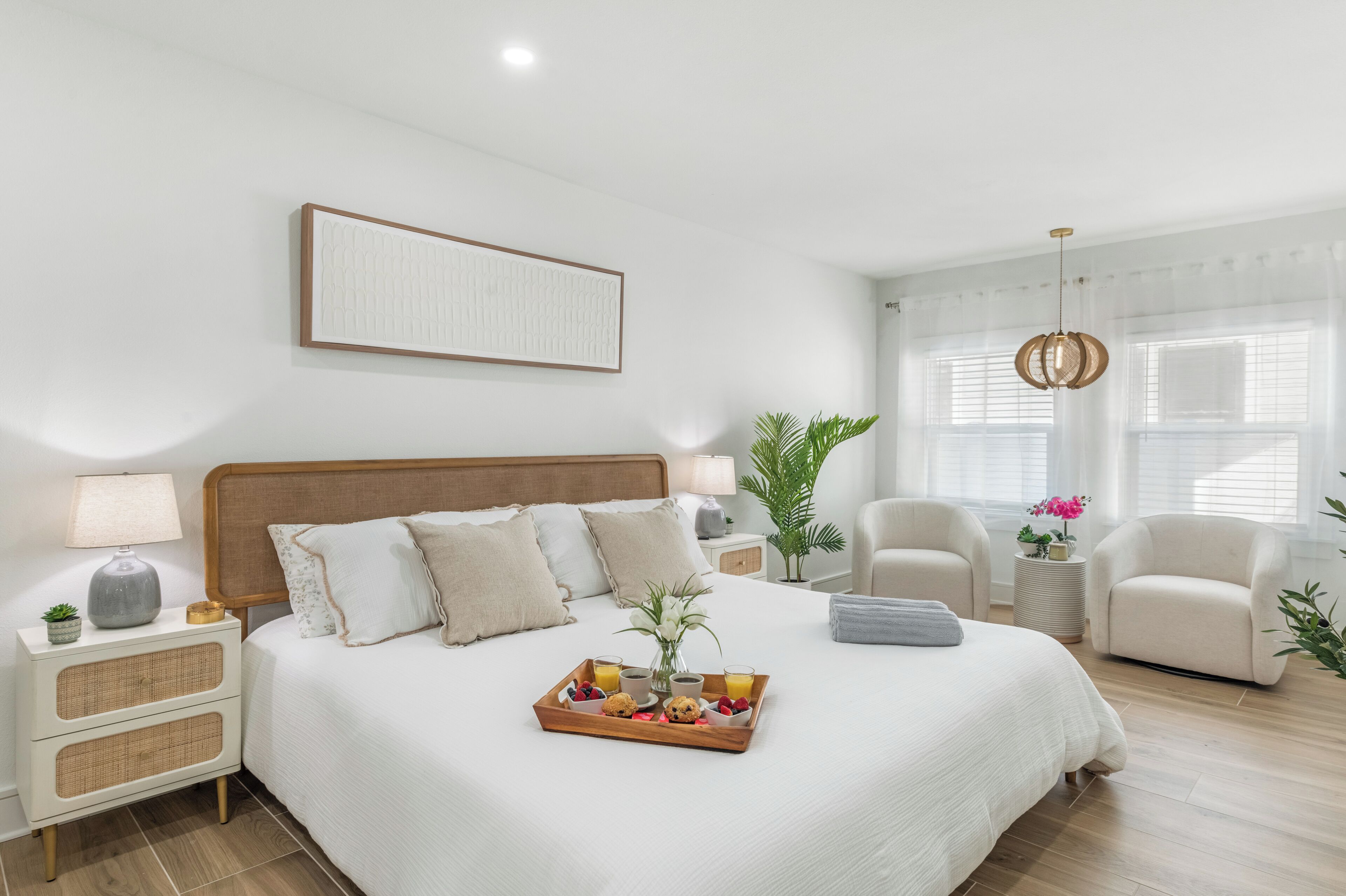 A modern bedroom with a large bed, bedside tables, a chair, a window with curtains, and a tray with breakfast items.