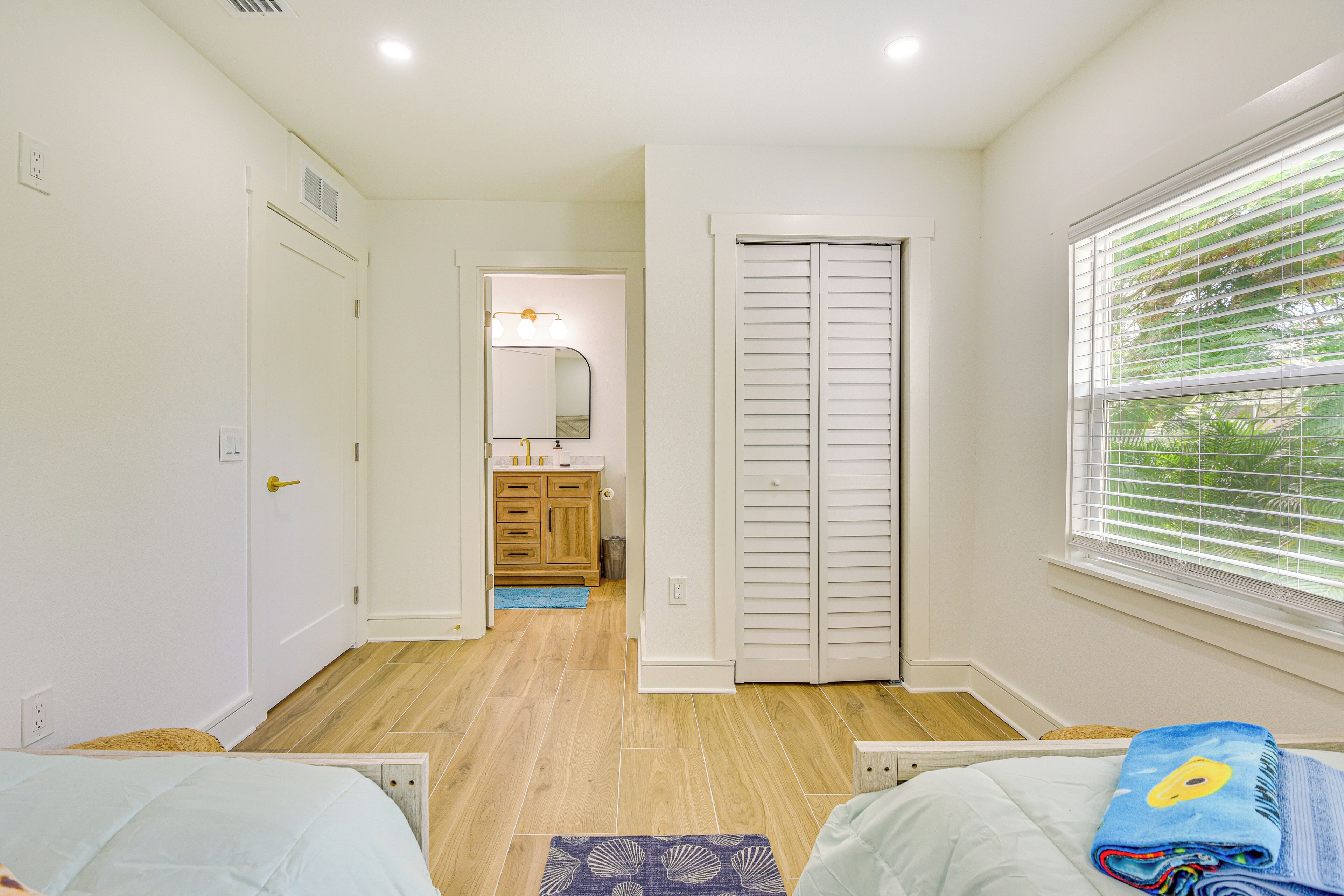 A bedroom with a bed, a window with blinds, a door, and a bathroom visible in the background.