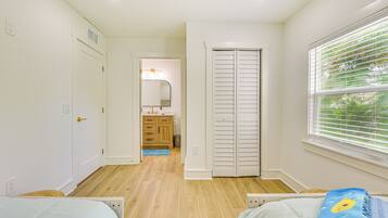 Une chambre à coucher avec un lit, une fenêtre avec des stores, une porte, et une salle de bain visible au fond.