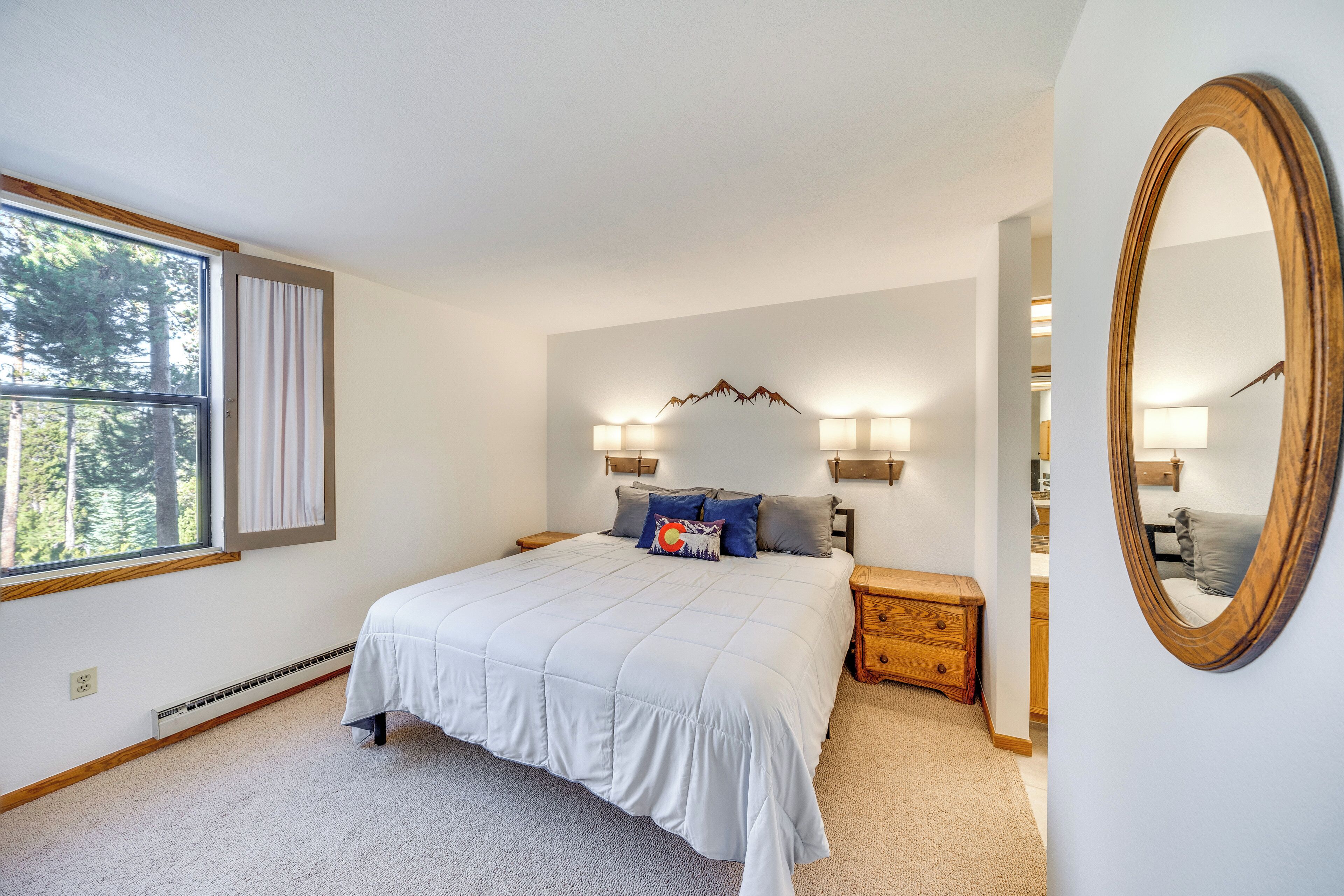 Une chambre à coucher avec un grand lit, des tables de chevet, un miroir et une fenêtre avec des rideaux.
