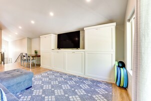Una sala de estar moderna con televisor de pantalla plana, armarios blancos, alfombra estampada y sofá azul.