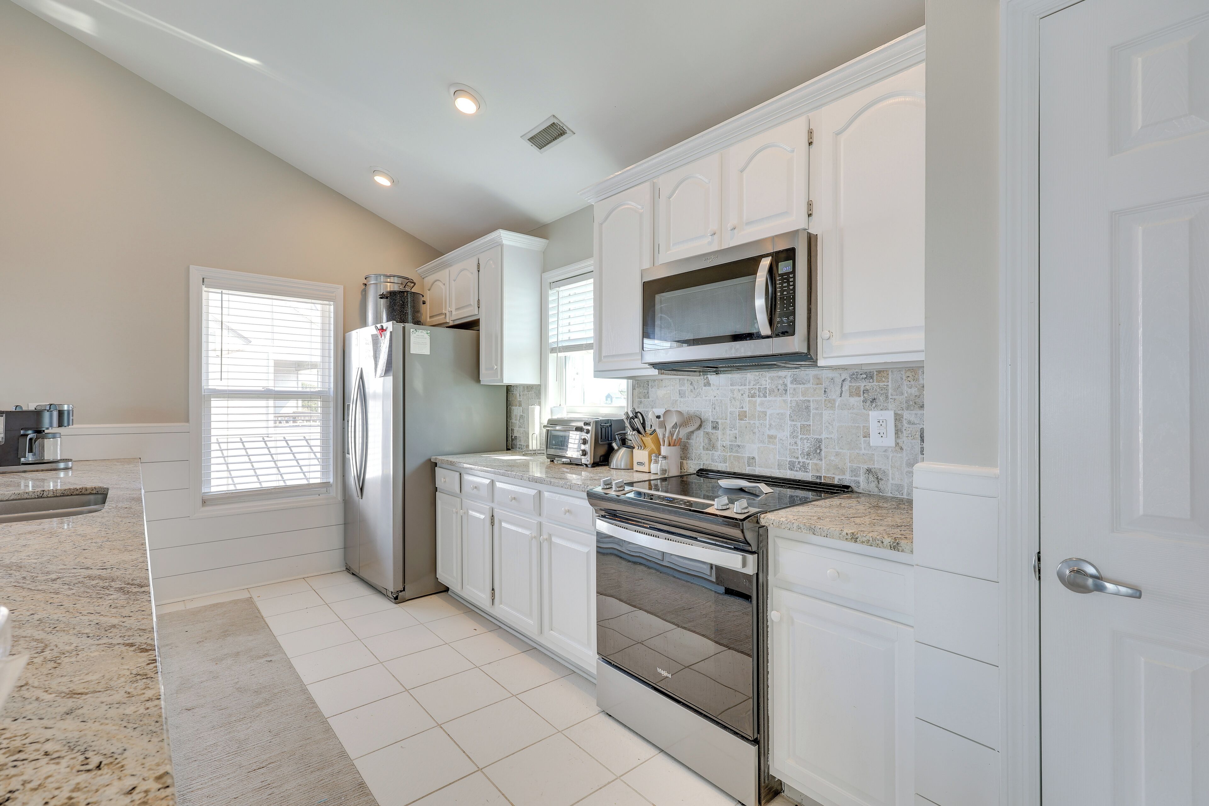 A modern kitchen with white cabinets, a stainless steel refrigerator, a microwave, and a built-in oven.