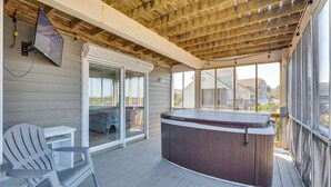 Een overdekt terras buiten met een hottub, een stoel en een tafel.