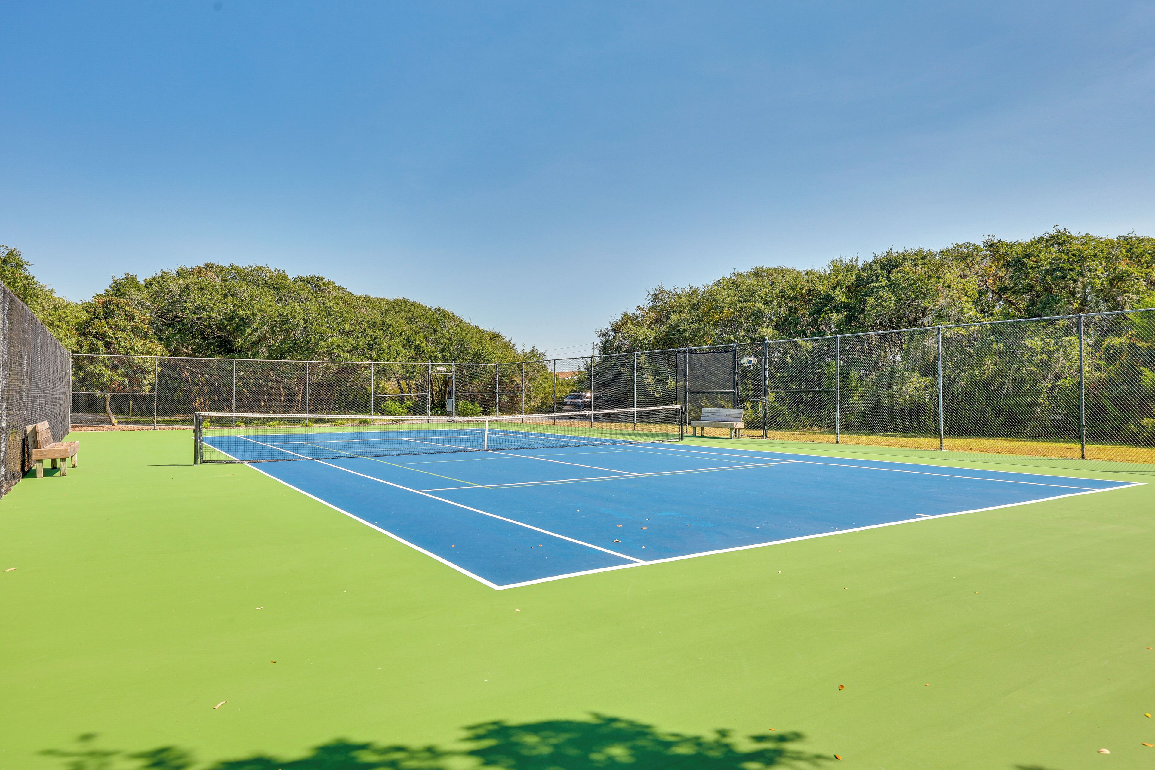 Un court de tennis avec un filet, entouré d’une clôture et d’arbres.