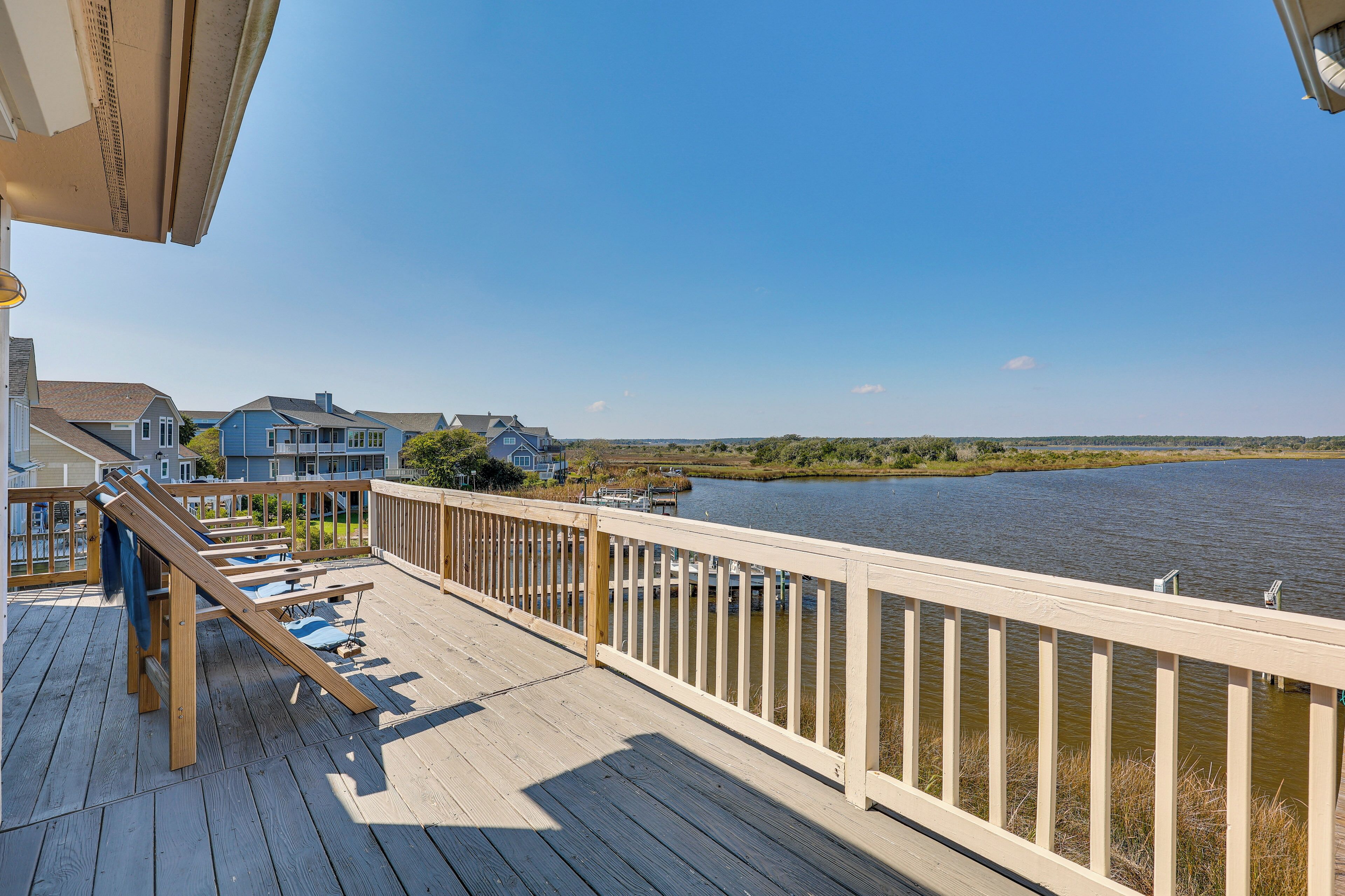 A wooden deck with a railing overlooking a body of water, with houses in the background.